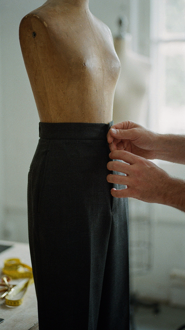 Tailor's hands meticulously adjust the hem of a dark wide leg pant.