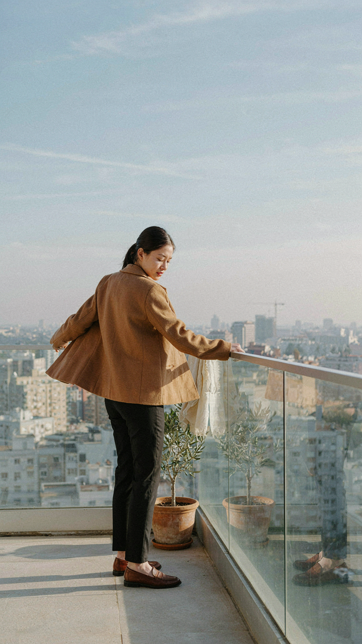 A person tests a structured wool jacket on a home balcony for wind behavior.