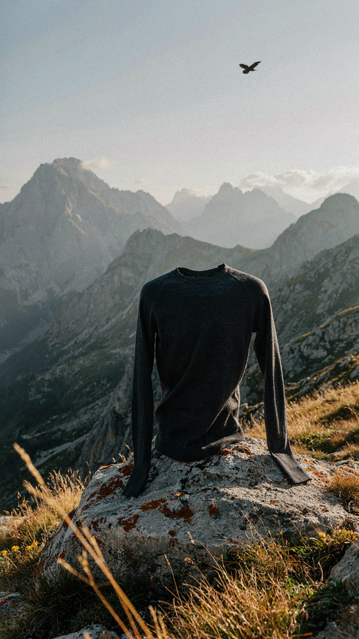 A durable merino wool shirt drapes over a rock in a stormy mountain setting.