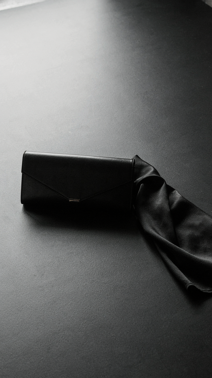 A black angular clutch rests beside a textured black satin garment, showing monochromatic depth.