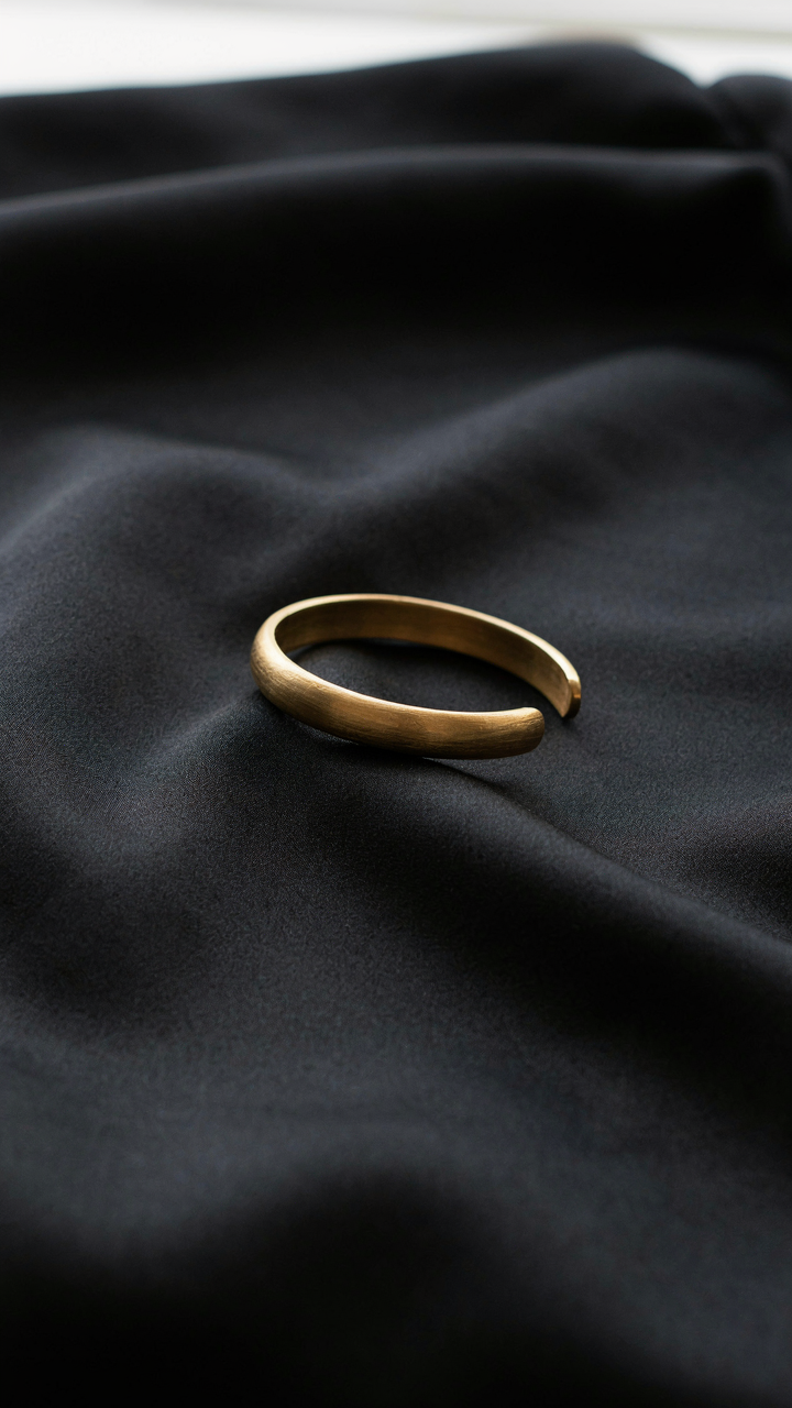 A brushed gold bracelet resting on a matte black silk dress.