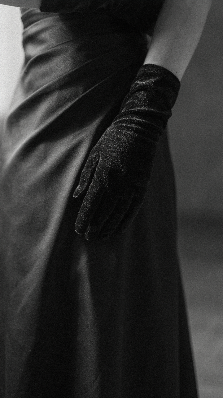 A hand in a black velvet long glove against a black silk dress.