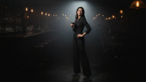 A woman in a black jumpsuit stands confidently in a cocktail lounge.