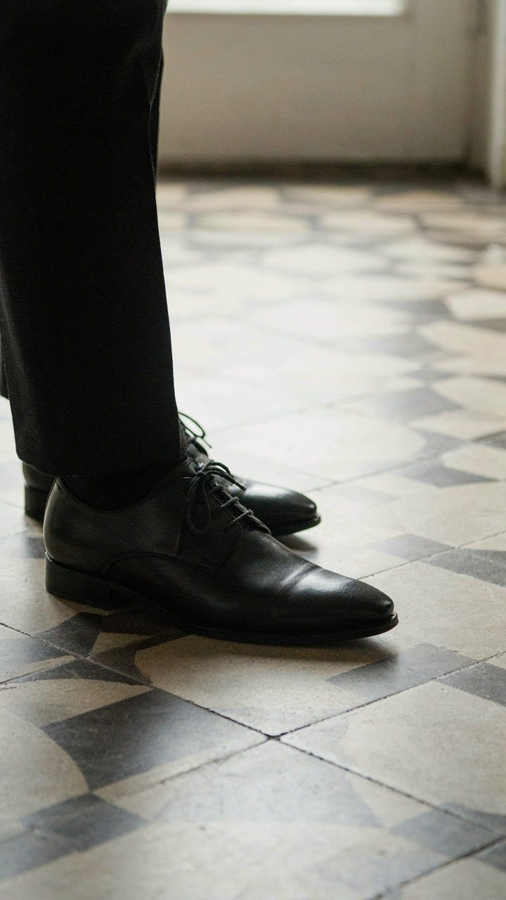 Close-up of a man's feet in a black suit and pointed toe black oxford shoes.