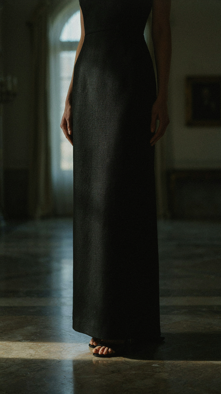 A person in a black jacquard weave gown stands in an elegant room.