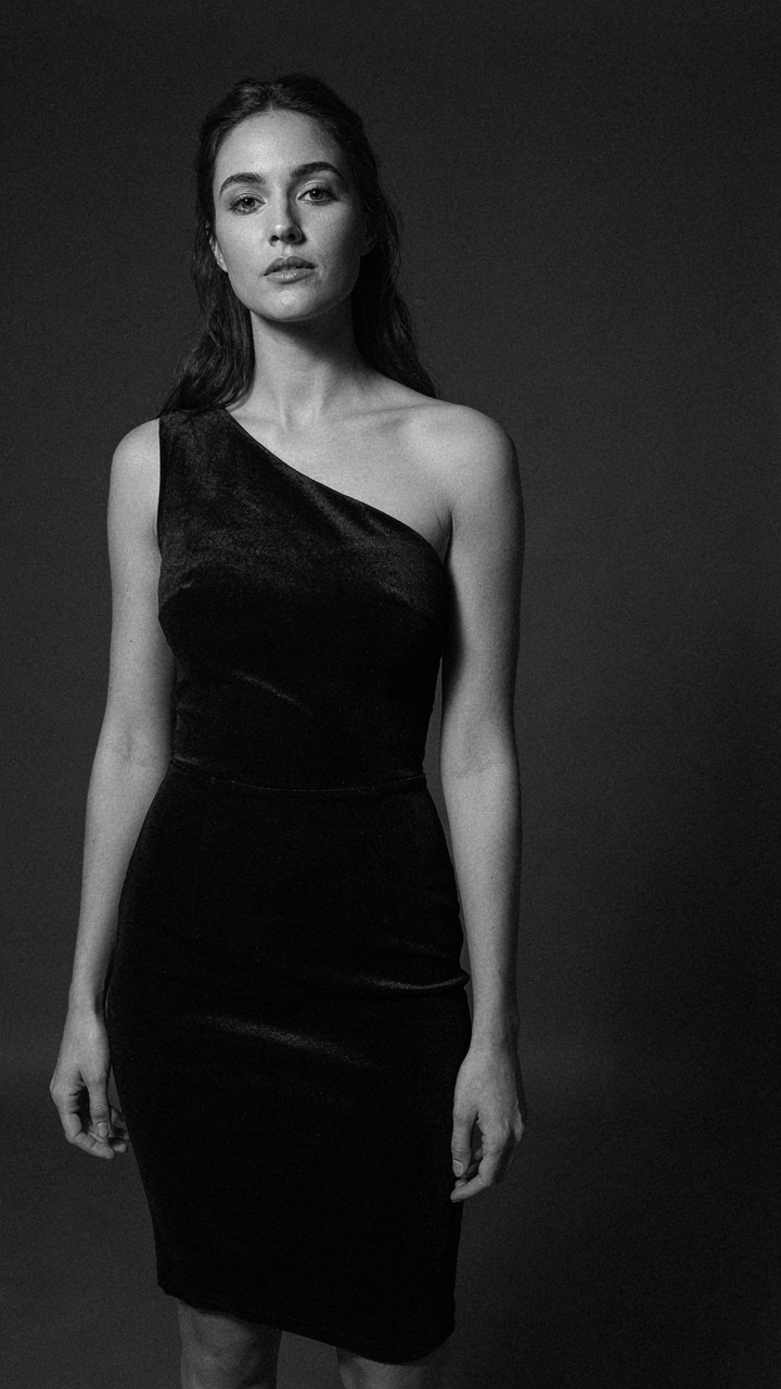 A woman wears a black velvet cocktail dress with an asymmetrical one-shoulder.