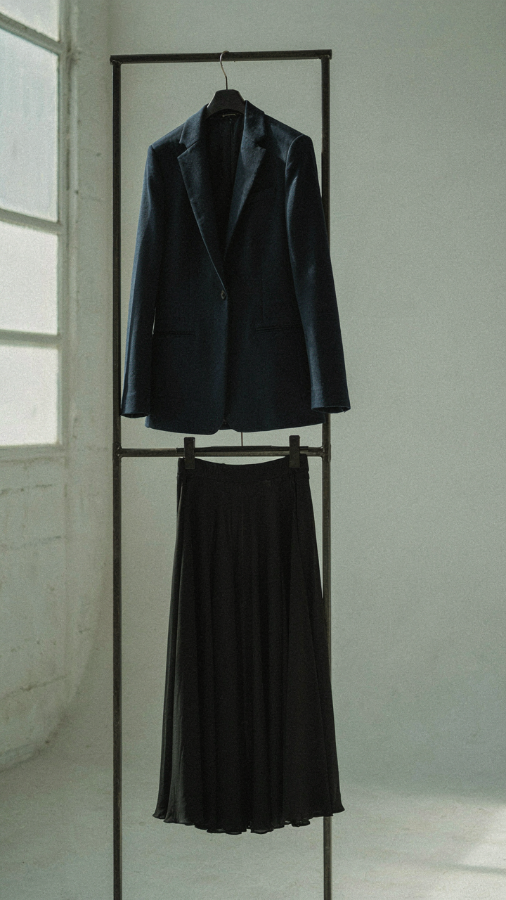 A tailored blazer hangs next to a flowing pleated skirt.