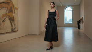 Woman in a black bow detail cocktail dress in an art gallery.