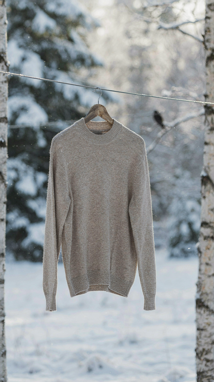 A merino wool sweater hangs on an outdoor clothesline in freezing air.