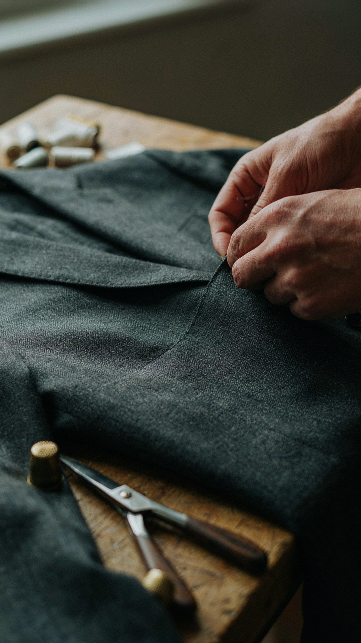 A tailor's hands closely inspect tight stitching on a high-quality wool blazer.