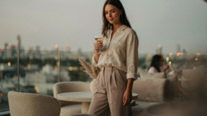 A person in stylish casual cocktail attire sips a drink at a relaxed evening party.