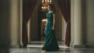 A woman in a beautiful jewel-toned gala dress walks into a grand ballroom.