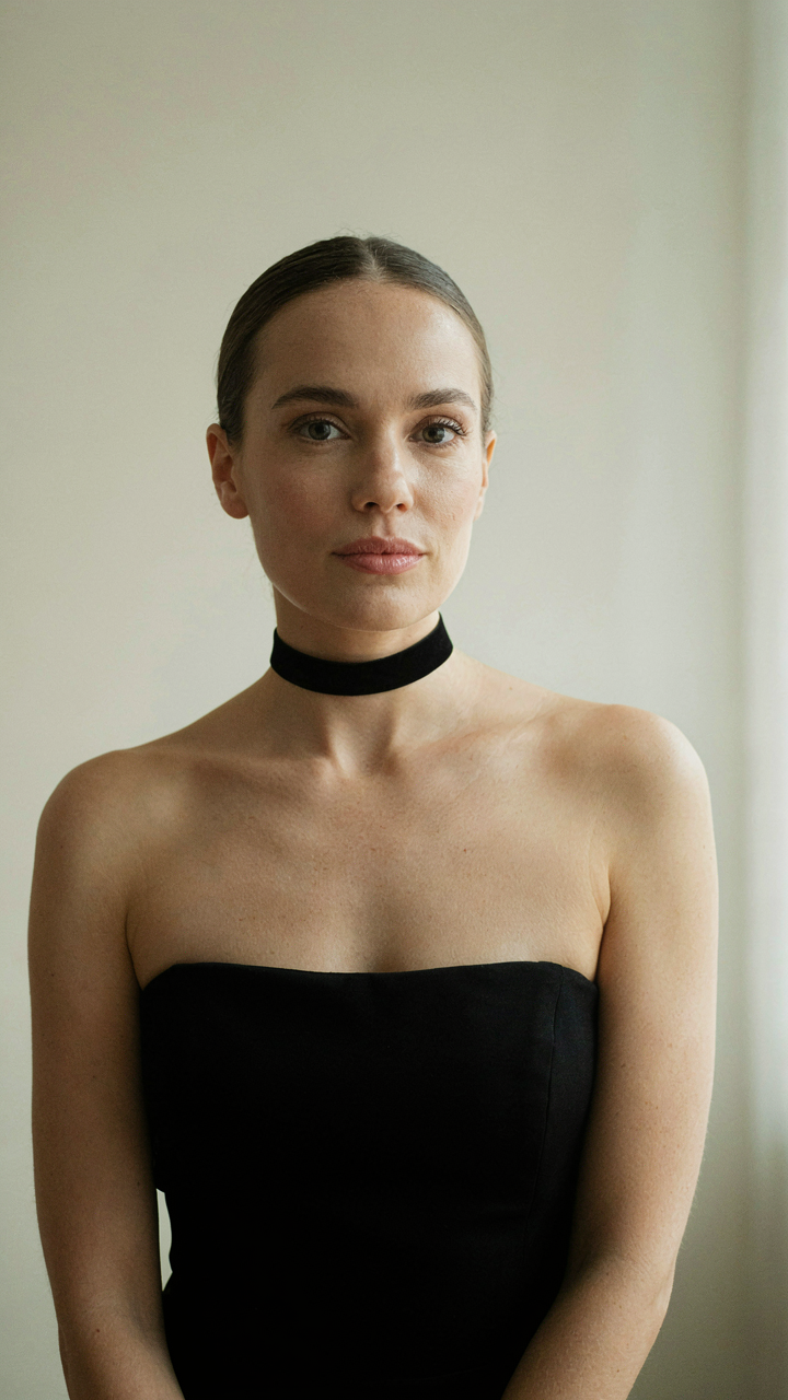 A woman wears a sleek black choker necklace that frames her face.