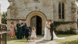 Well-dressed wedding guests, in various church wedding guest dress styles, arrive at a stone church.