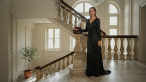 A woman in a classic black tie gown stands at the top of a grand staircase.