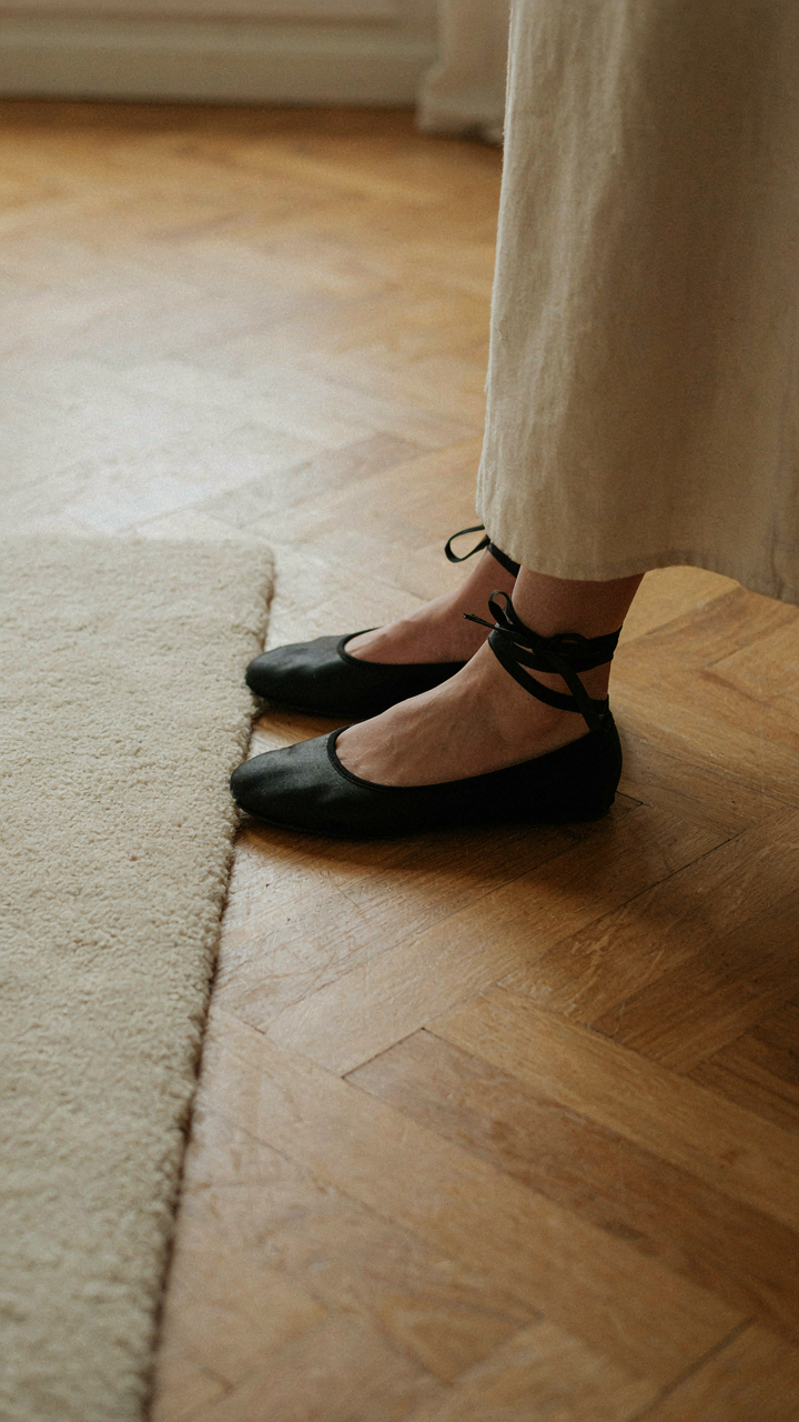 A woman's feet in elegant black satin ballet flats with ribbon detail.