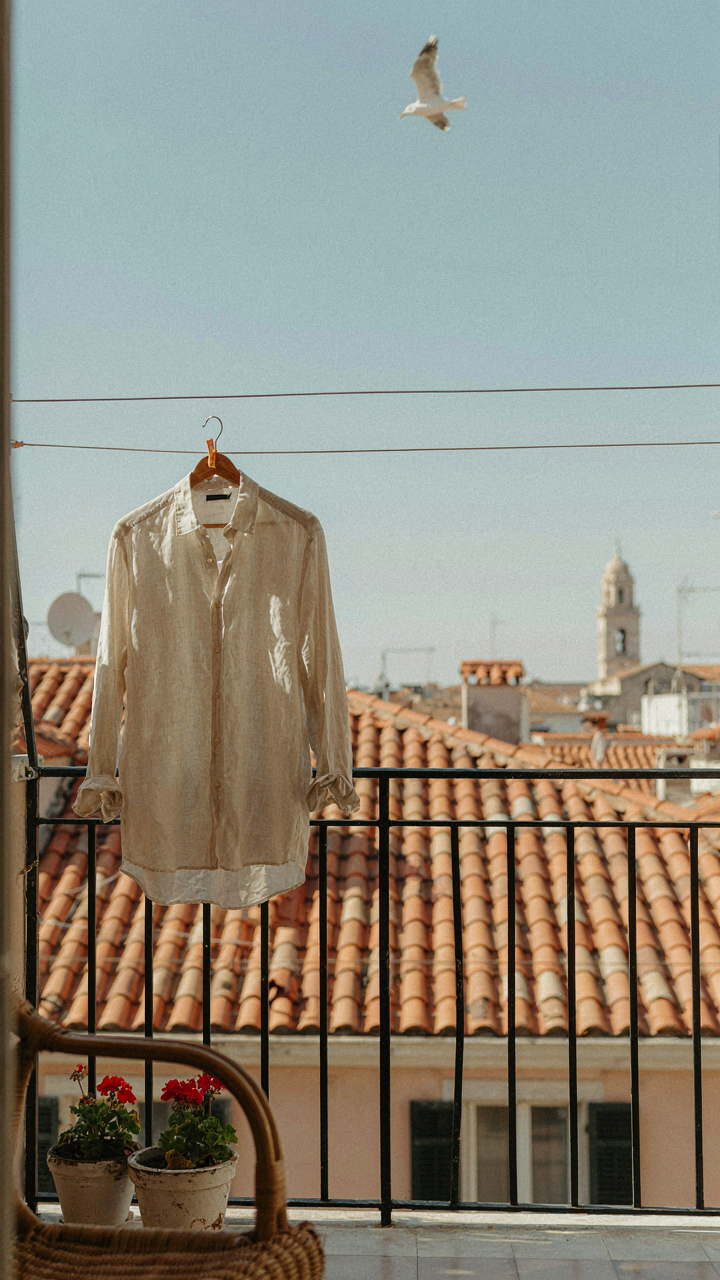 A linen shirt dries on a clothesline on a sunny hotel balcony.