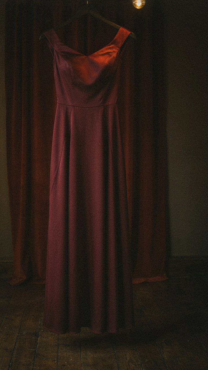 A burgundy satin cocktail dress glows softly in a warm-toned room.