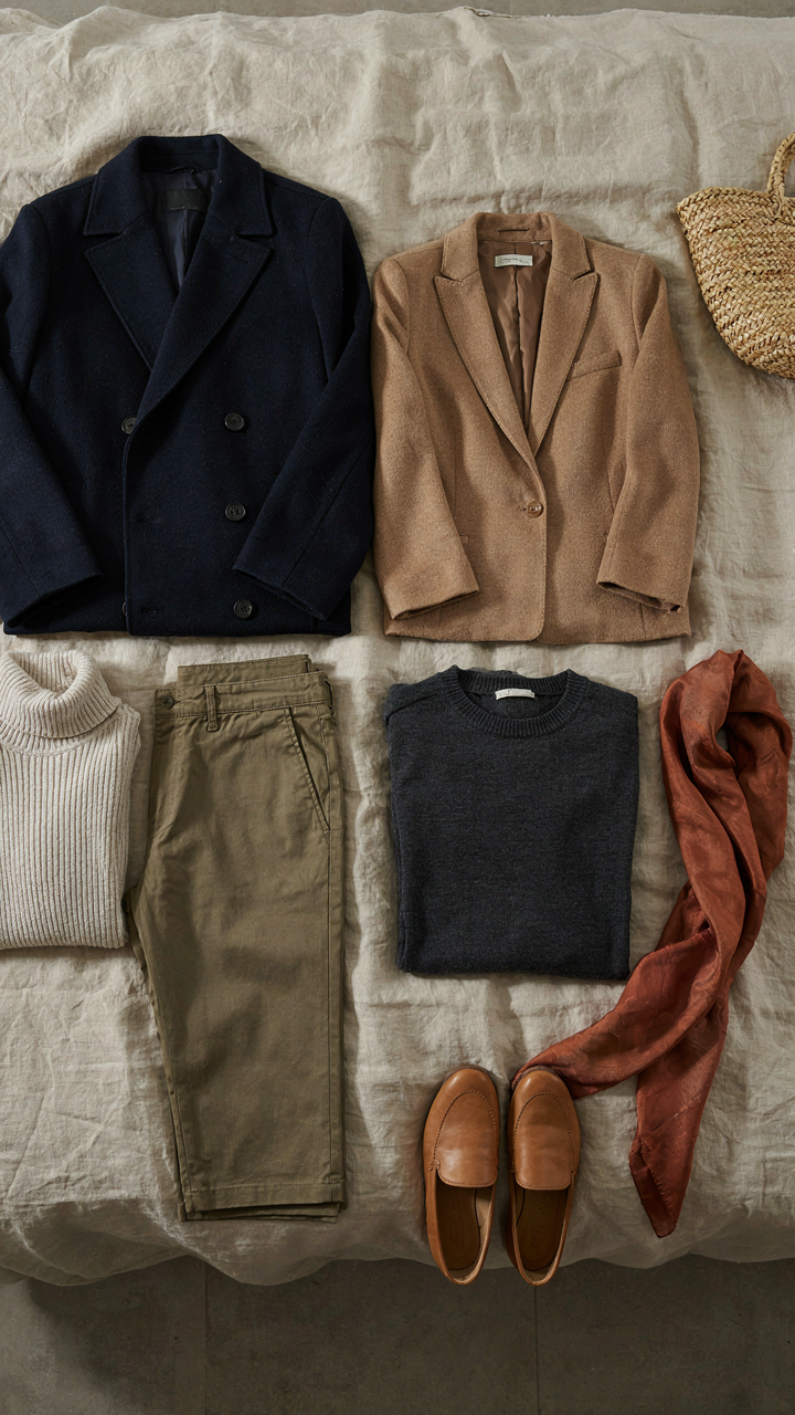 Coordinated neutral clothing items with a muted accent scarf on a bed.