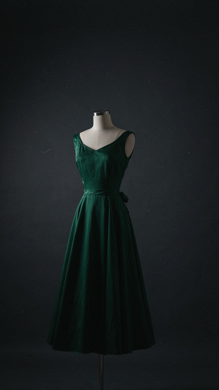 Emerald green silk 1950s style cocktail dress shimmering under a spotlight.
