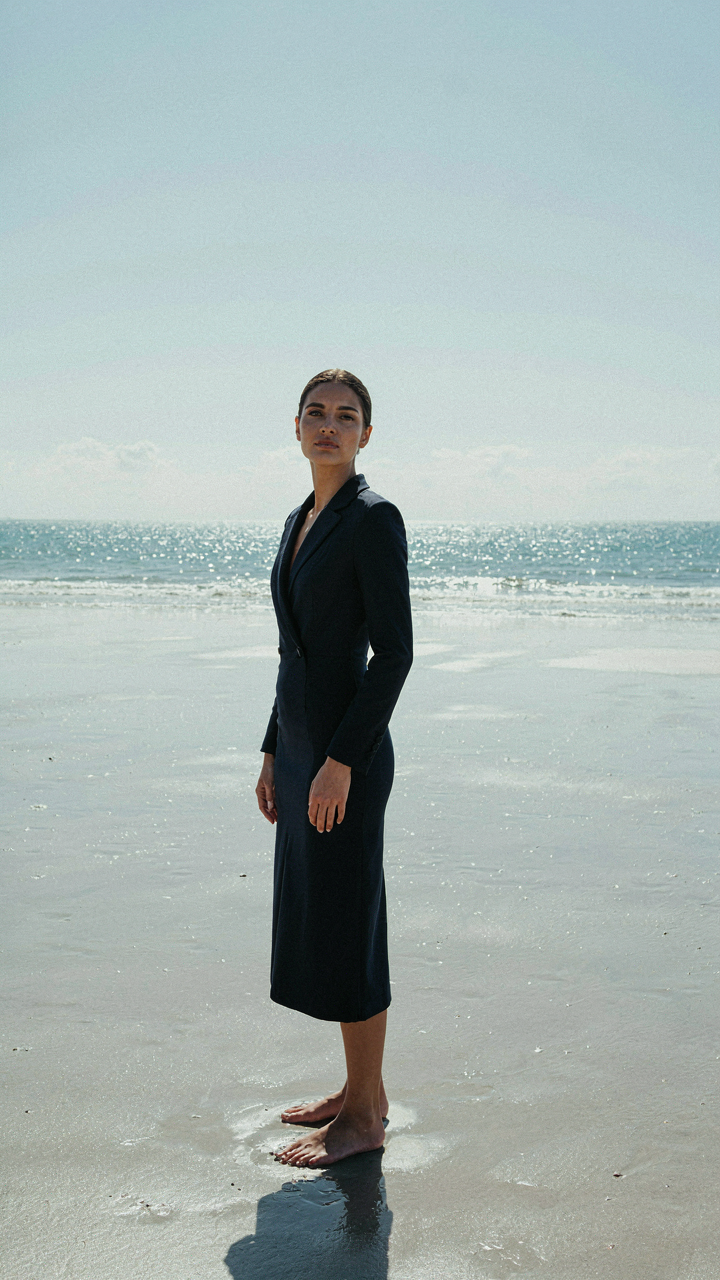 Woman in a rich navy blue dress standing on bright, reflective sand.