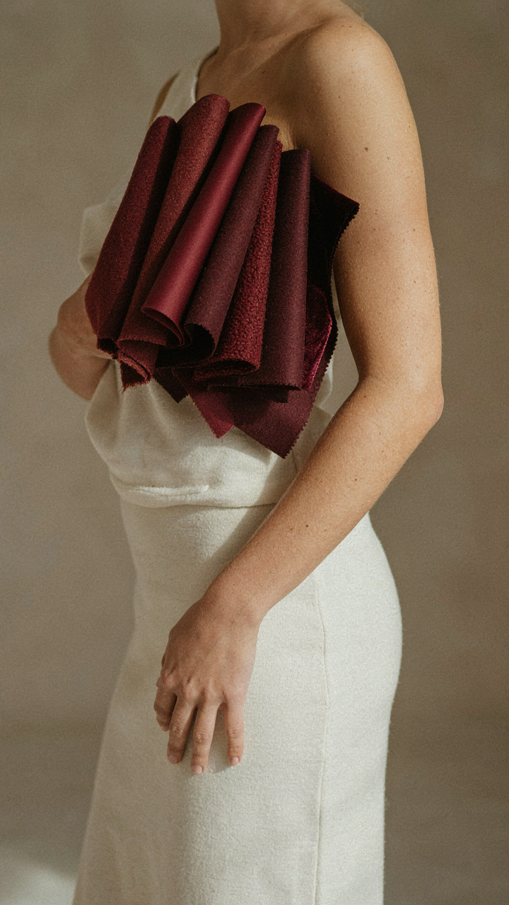 A hand holds burgundy fabric swatches against a warm skin tone arm.
