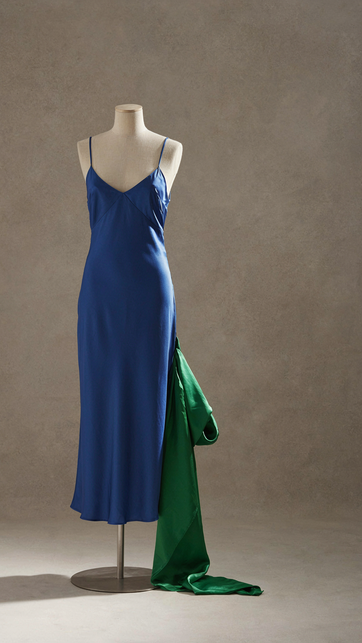 A sapphire blue dress on a mannequin with an emerald green scarf nearby.
