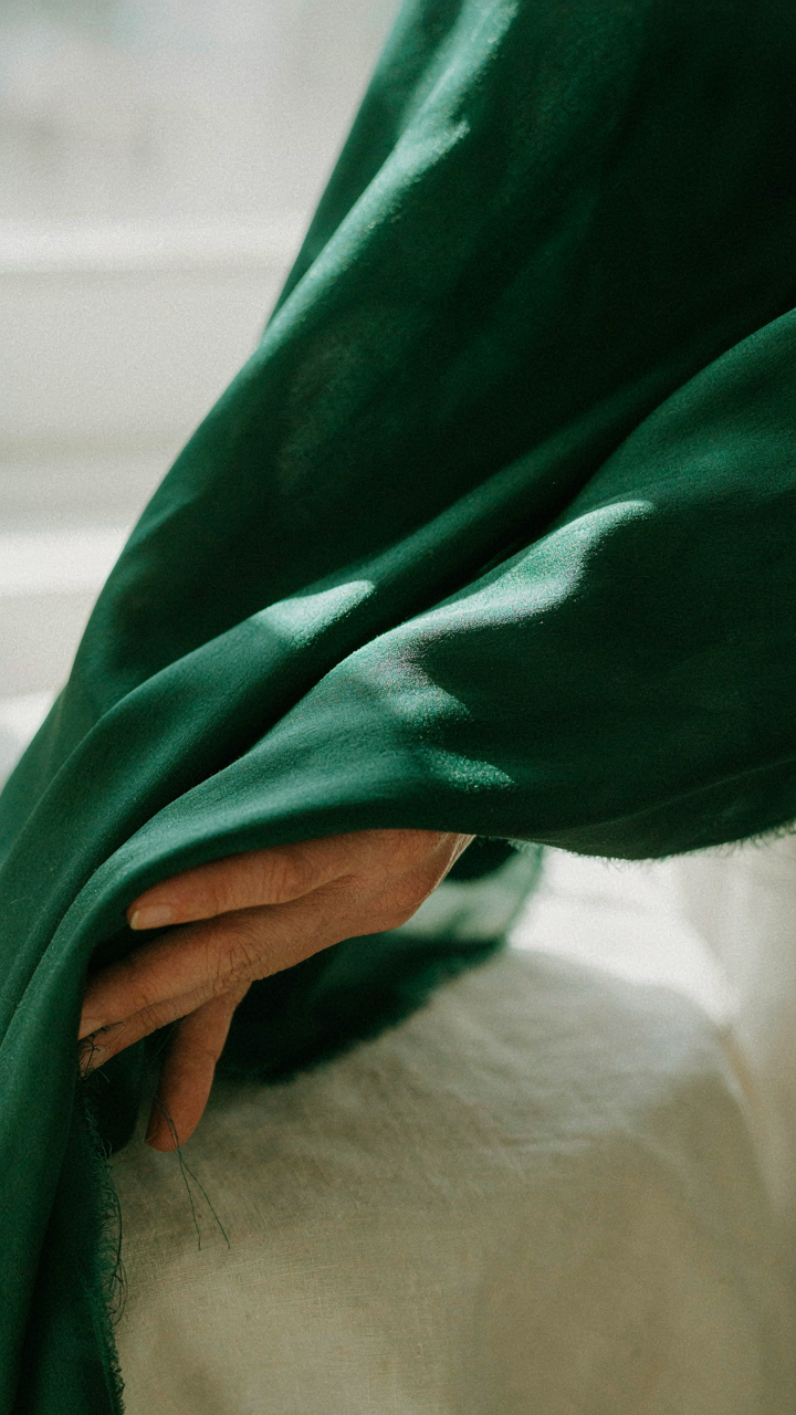A close-up of deep emerald green silk fabric draped over a hand.