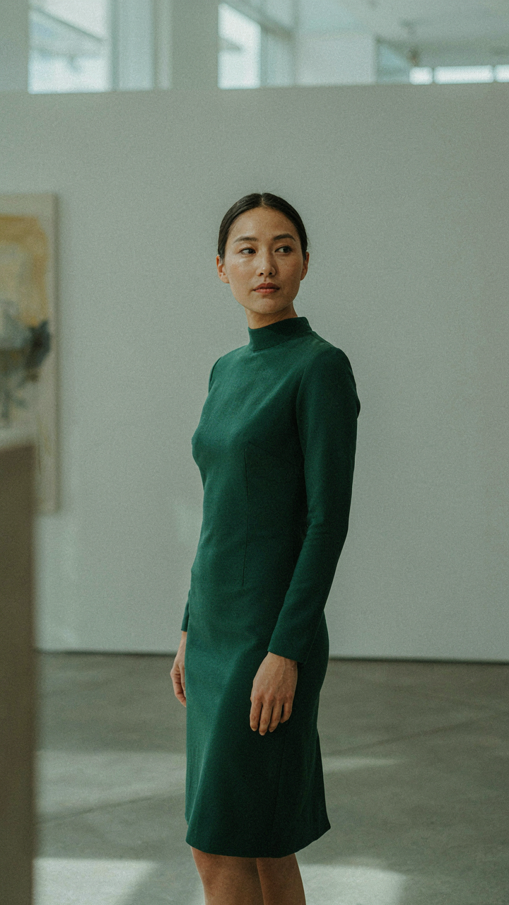 A woman in an emerald green high neck cocktail dress in an art gallery.