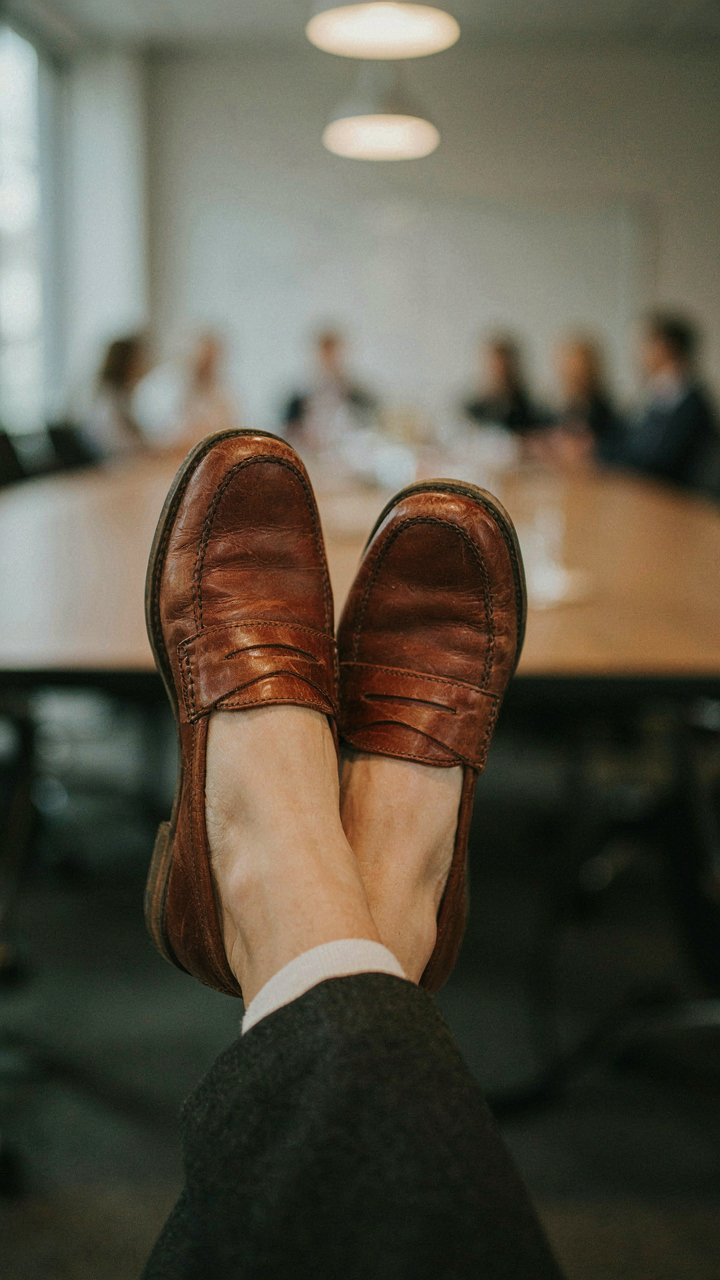 A woman's feet wear comfortable, polished leather loafers under a conference table.