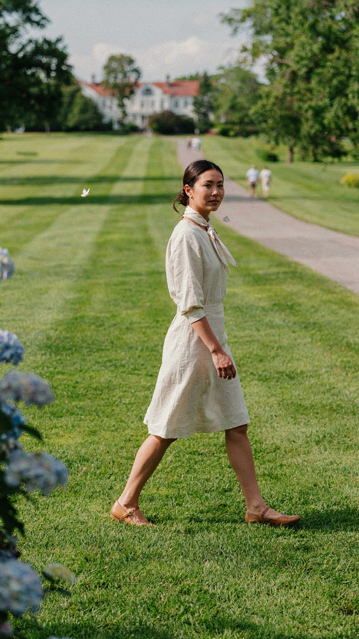 A woman in a simple linen dress, silk scarf, and flats walks at a country club.