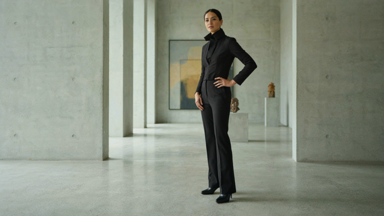 Woman in a structured jumpsuit in a modern gallery, embodying creative black tie attire.
