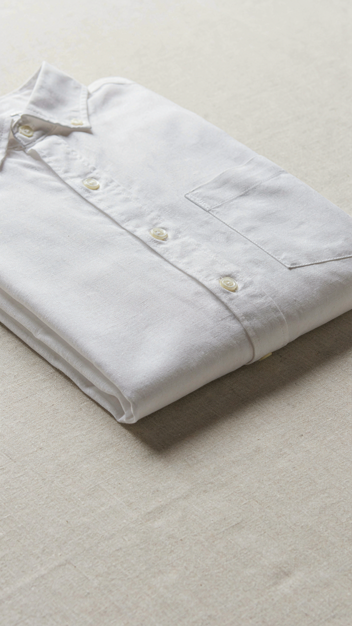 A close-up shows a neatly folded white oxford shirt with visible fabric texture.