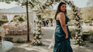 Curvy woman in a deep teal dress confidently posing at a wedding.