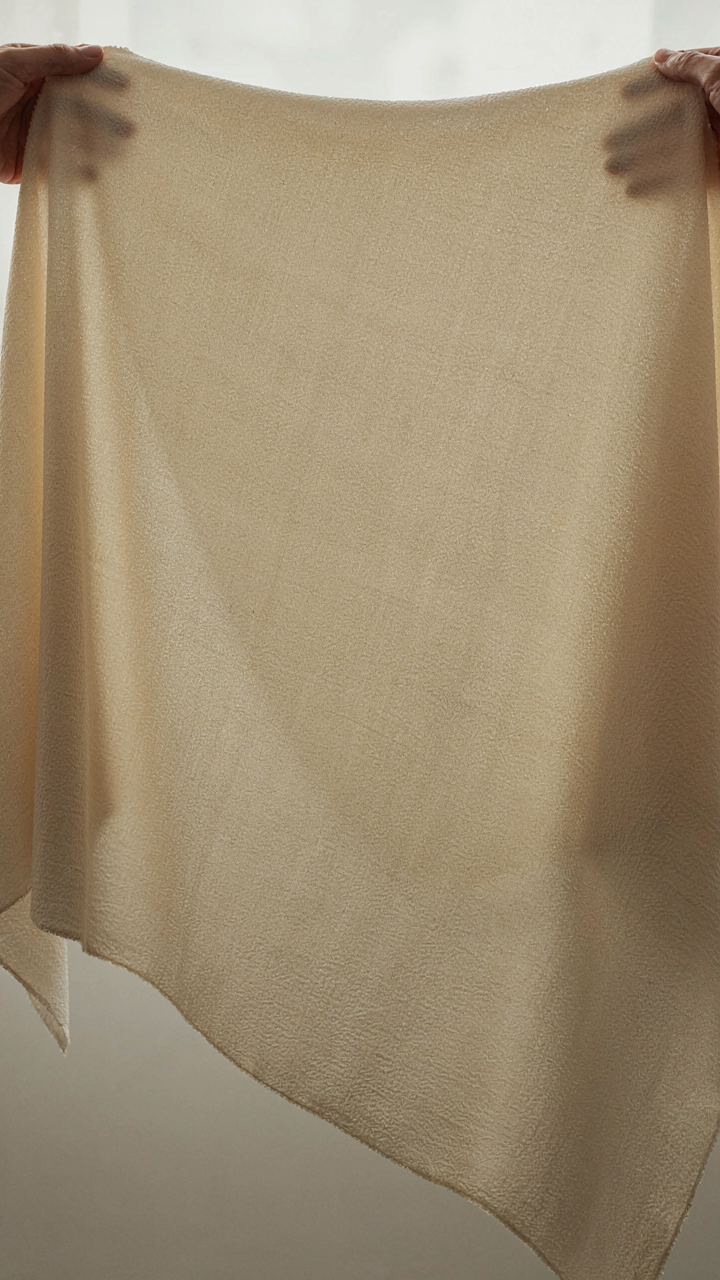 A hand holding up a piece of structured crepe fabric, highlighting its quality.