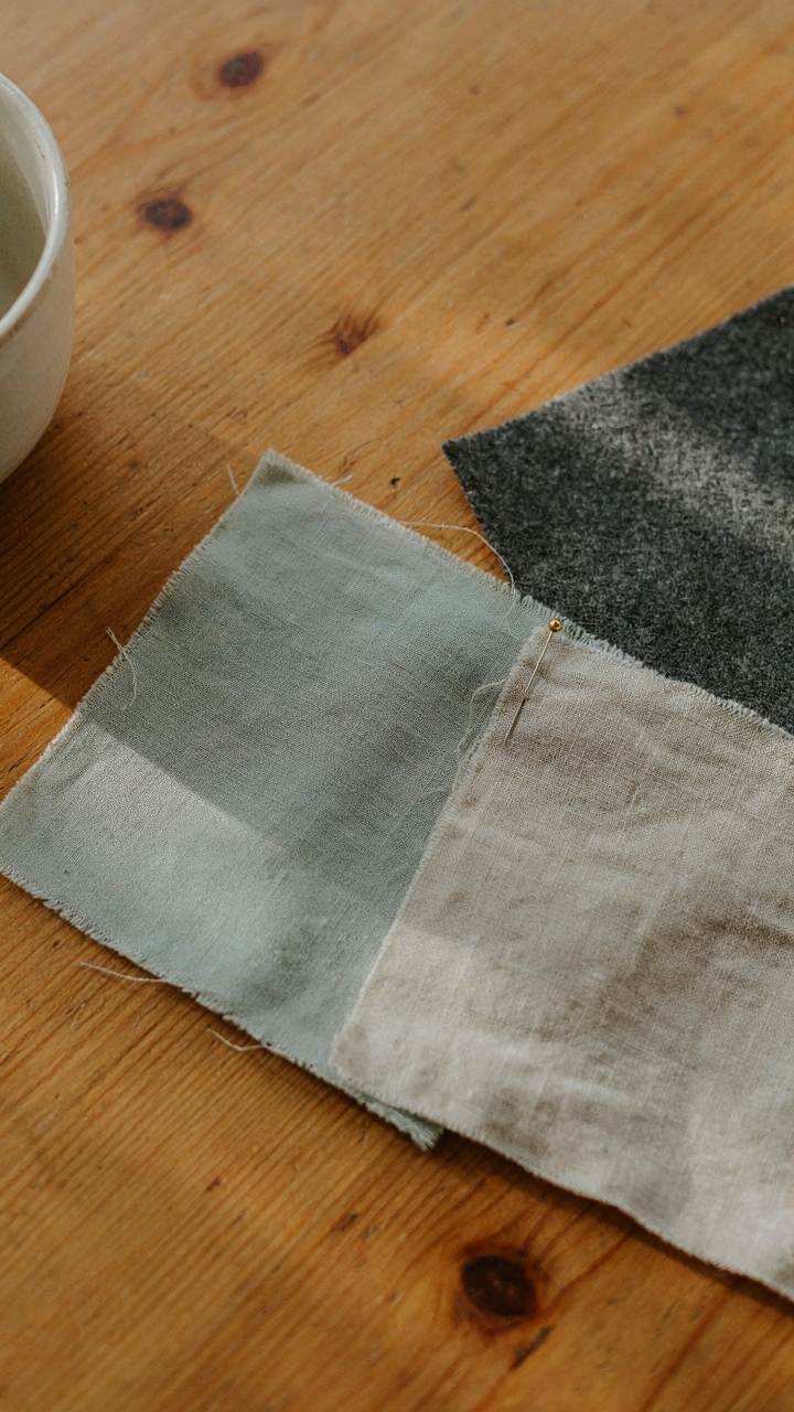 Matte fabric swatches in sage, beige, and charcoal sit on a sunlit wooden table.