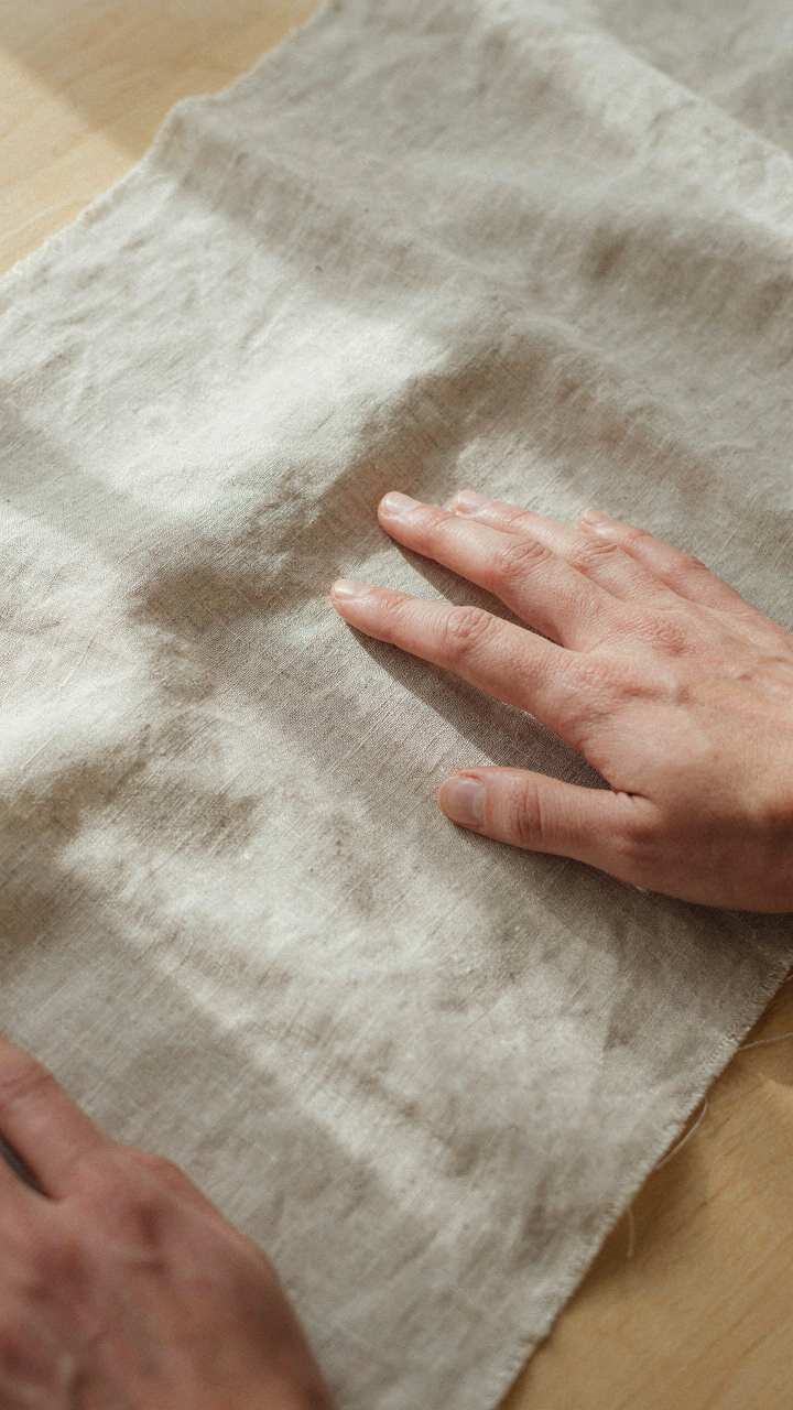 A hand touches a finely textured, intentionally wrinkled linen fabric.