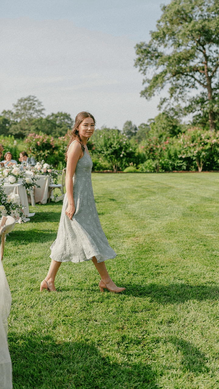 Woman in a breathable dress and low heels walks on grass at a garden wedding.