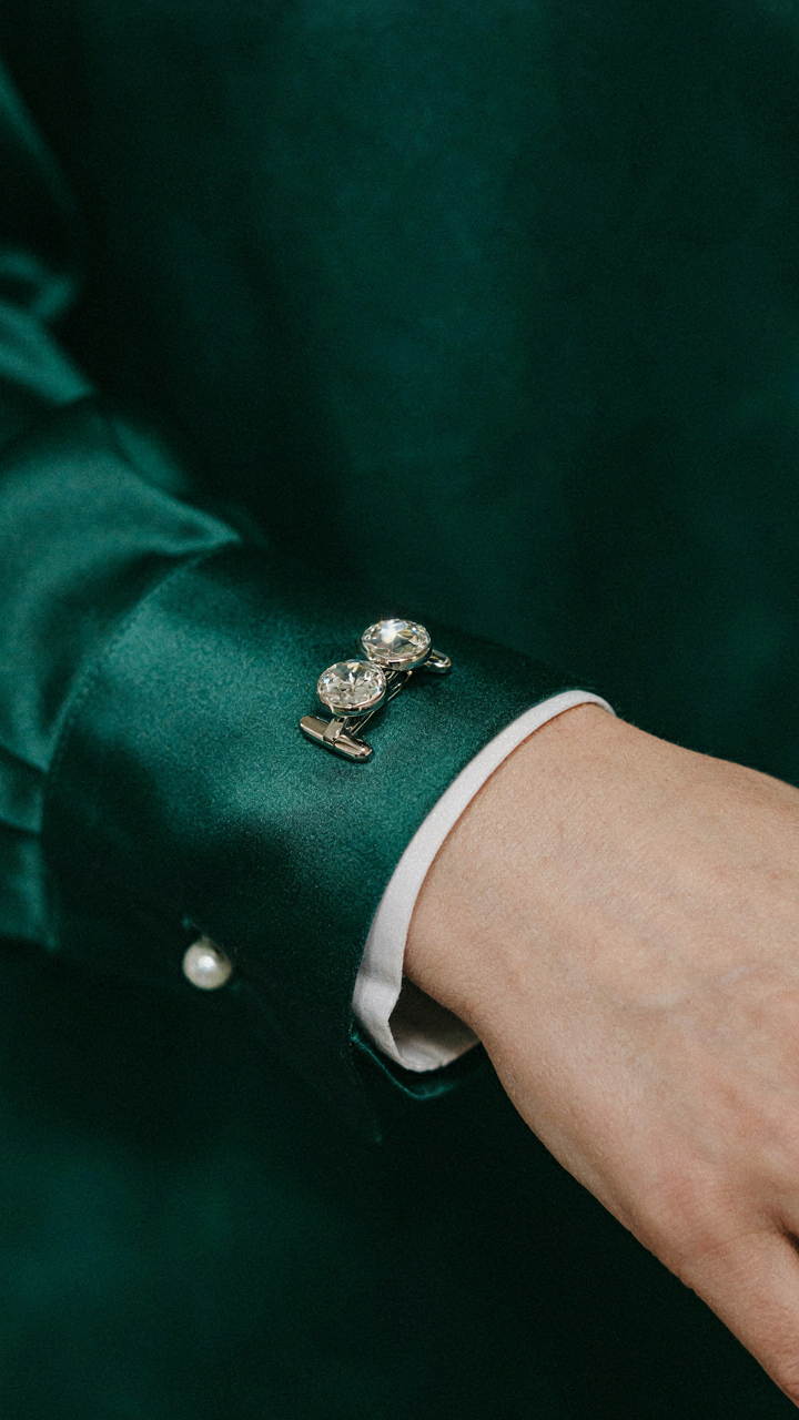 Close-up of metallic cufflinks on a deep emerald silk blouse.