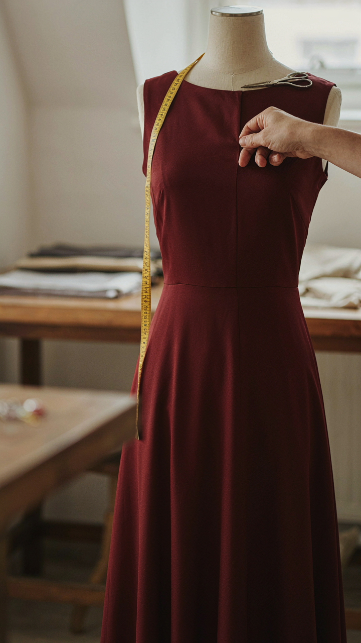 A tailor adjusts the vertical seam of a burgundy midi cocktail dress.