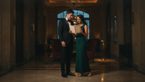 A man in a tuxedo and a woman in a cocktail dress look at an event invitation.