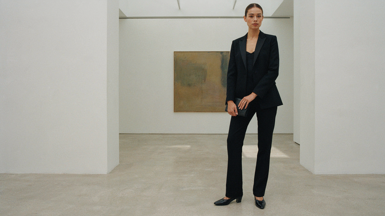A person in a sharp black cocktail outfit stands in a modern art gallery.