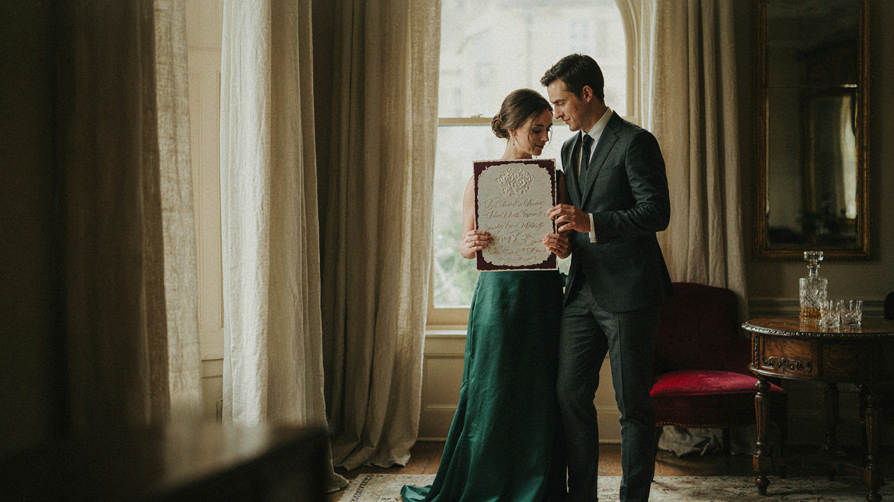 A formal couple looking at a wedding invitation with a printed dress code.