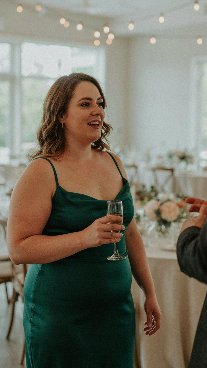 A smiling plus size wedding guest enjoys a conversation at a reception.