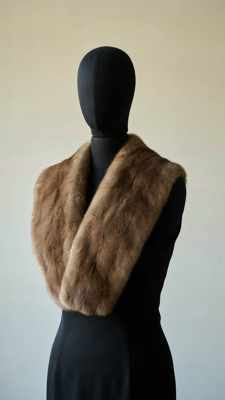 A mink fur stole draped over a black cocktail dress on a mannequin.