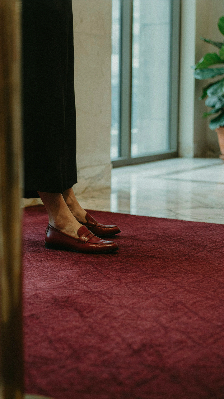 A person in polished loafers steps onto a plush carpet in a fancy lobby.