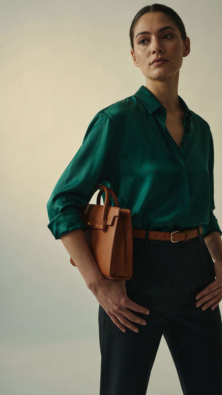 A woman wears a jewel-toned blouse with a leather belt and structured handbag.