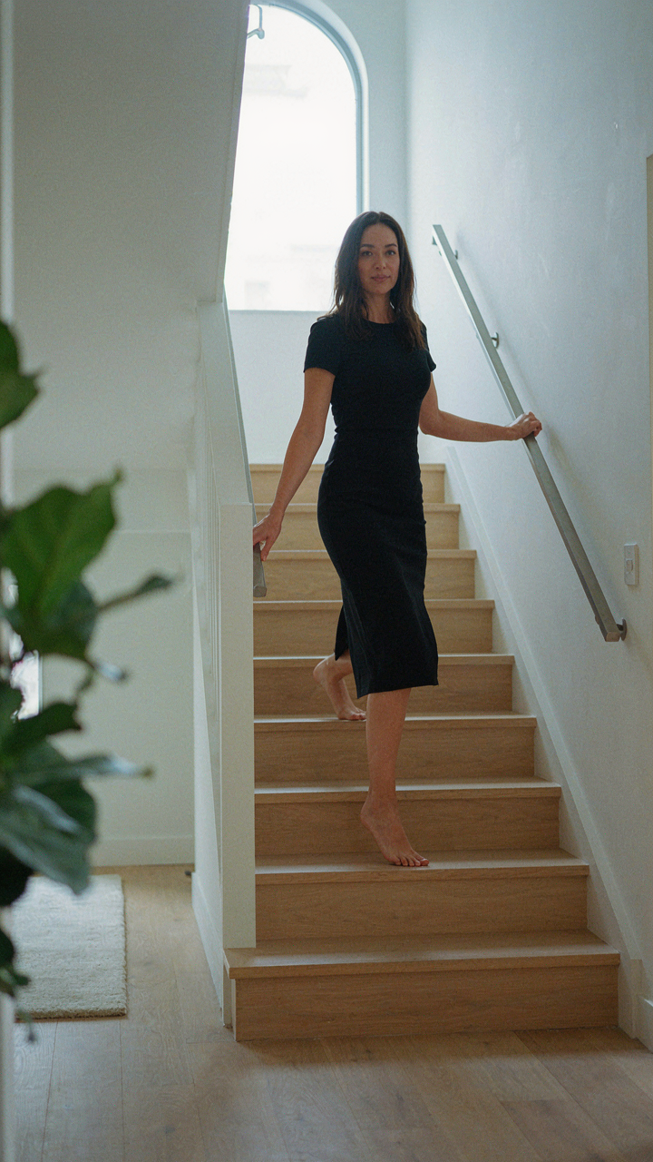 A woman in a black midi cocktail dress easily walks up stairs.