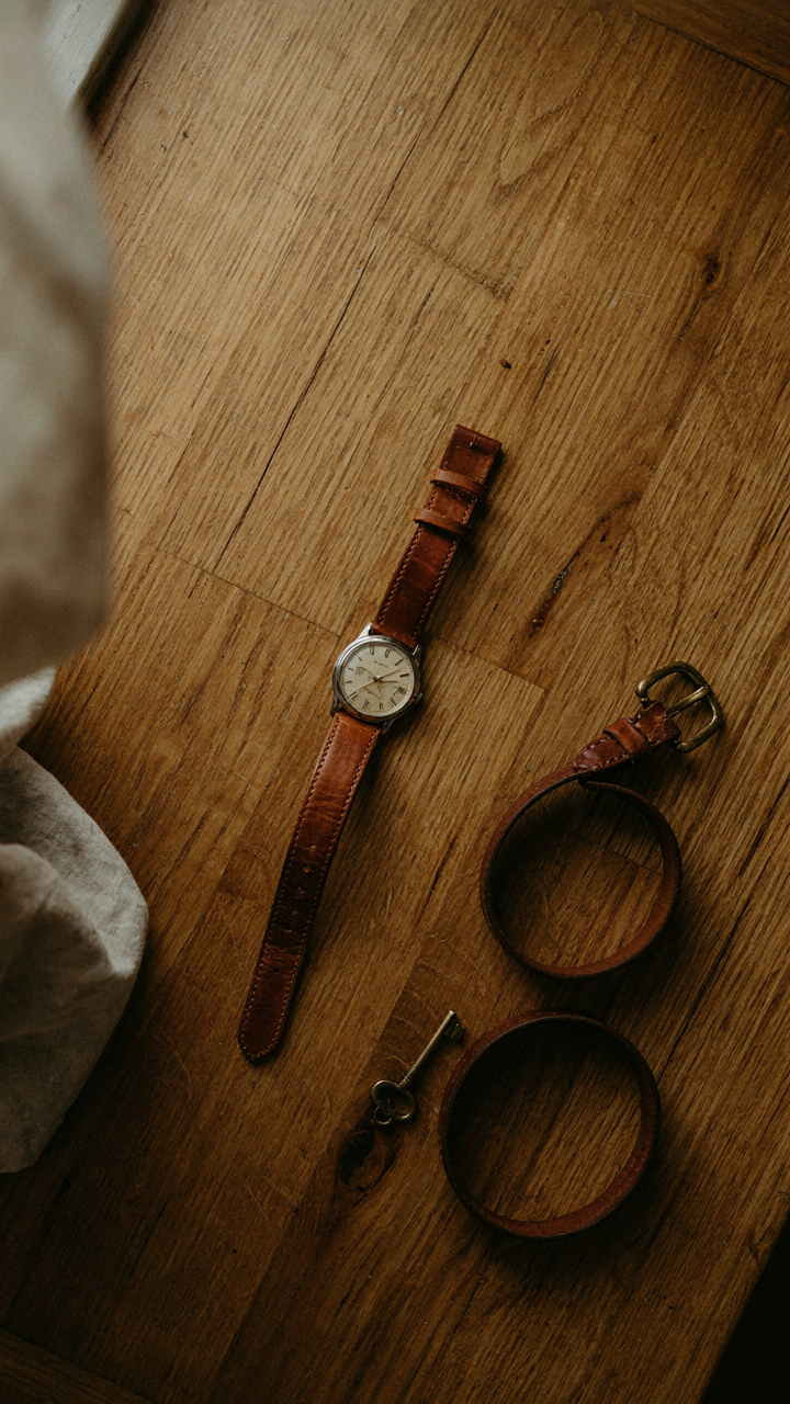 A brown leather watch and matching leather belt rest on a wooden surface.