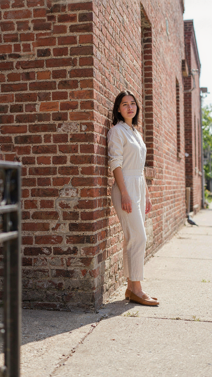 Person in a jumpsuit stands in a brick building corner, lines converging.